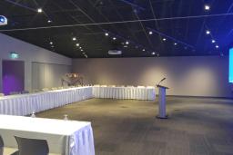 A large room containing a long C-shaped table on the left that can seat around 30 people, facing a podium to the right.