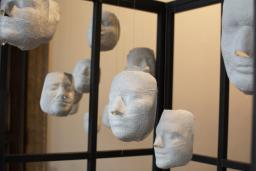 Several white plaster faces hang from strings, inside a cage.