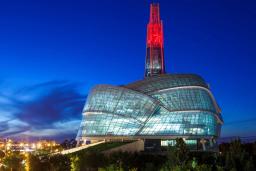 A huge building with a rounded glass façade is topped by a glowing red tower.