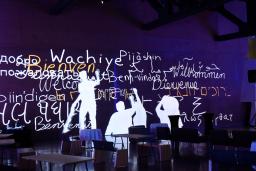 Interactive screen depicts human figures writing “welcome” in several different languages.