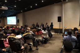 A panel of five people are seated in front of a large crowd inside the Canadian Museum for Human Rights.