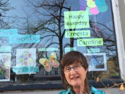 A woman sitting outside in front of a large picture window decorated with colourful signs.