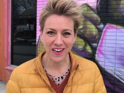 A woman facing the camera with a colourful mural behind her.