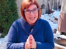 A red-haired woman wearing a blue jacket sitting in a snow-covered garden.