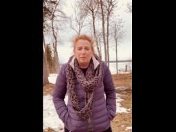 A woman in a winter coat standing outside in a partly snow-covered park.