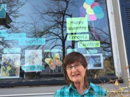 A woman sitting outside in front of a large picture window decorated with colourful signs.