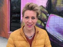 A woman facing the camera with a colourful mural behind her.