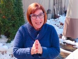 A red-haired woman wearing a blue jacket sitting in a snow-covered garden.