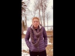 A woman in a winter coat standing outside in a partly snow-covered park.