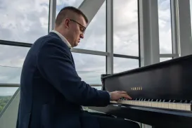 A male musician dressed in a dark blue suit is sitting and playing the piano.