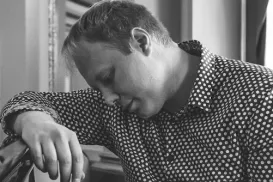 A male musician is sitting at a piano with his left index finger on a piano key.