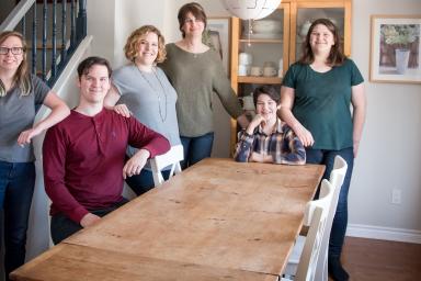 A smiling family of six gathered around a dining room table.