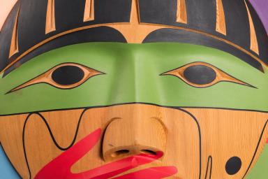 A carved wooden box, showing the carved face of a person with a painted red hand over their mouth.