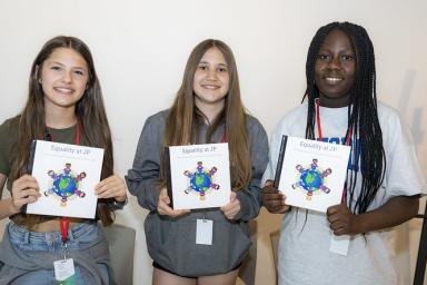 Three students hold copies of a book that they've created. The book cover has a title that says "Equality at JP" and has a drawing of the earth with students all around it.