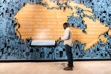 A man stands in front of an illustrated blue and orange a map of Canada.