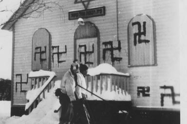 Two people play hockey in front of a synagogue with several swastikas painted on it.