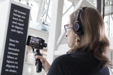 A woman holds a bar with a mobile phone attached to it and uses the screen to look at something off camera.