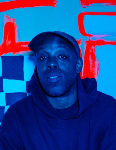 A blue-toned image of a black man wearing a cap and dark hoodie in front of a checkered backdrop with thick red lines. Partially obscured.