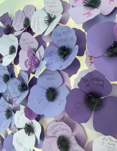 Purple poppies made of paper with names and messages from community members and family of those who have died as a result of a poisoned drug supply. Partially obscured.