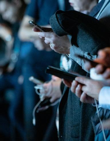 A group of people using cell phones while standing. Partially obscured.