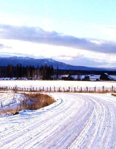 A snow-covered country road with mountains in the background. Partially obscured.
