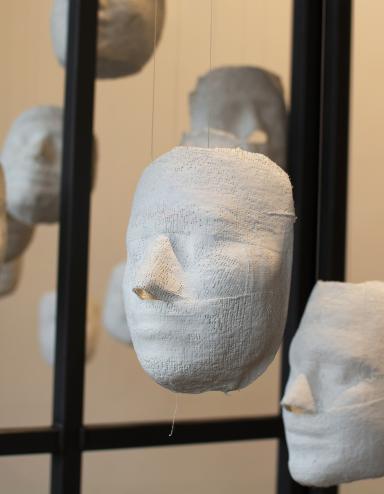 Several white plaster faces hang from strings, inside a cage. Partially obscured.