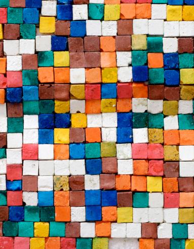 Square tiles of various colours and placed randomly are photographed from above, creating a pixellated effect. Partially obscured.