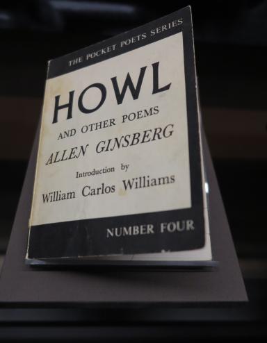 A book on display. The cover reads: The Pocket Poets Series. Howl and Other Poems. Allen Ginsberg. Introduction by William Carlos Williams. Number Four. Partially obscured.