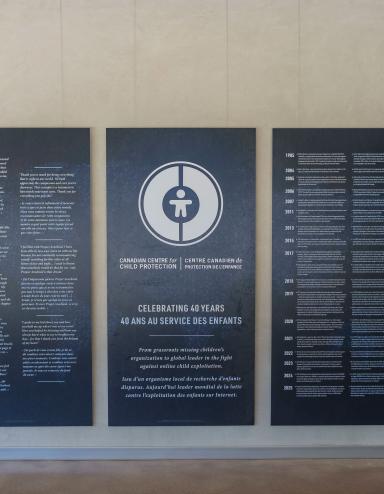 Large dark blue panels with white text and graphics displayed in the Community Corridor at the Canadian Museum for Human Rights. The centre panel features a circular logo and commemorates the 40th anniversary of the Canadian Centre for Child Protection. The two panels on either side present bilingual text in English and French. Partially obscured.