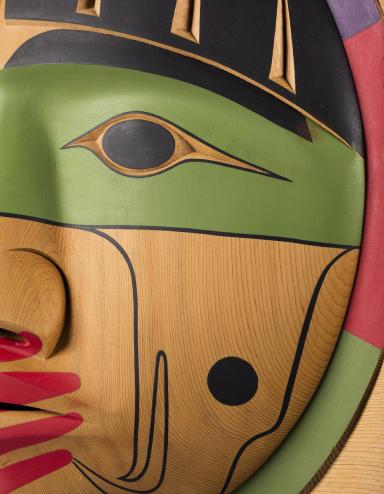 A closeup of a carved wooden box, showing the carved face of a person with a painted red hand over their mouth. Partially obscured.