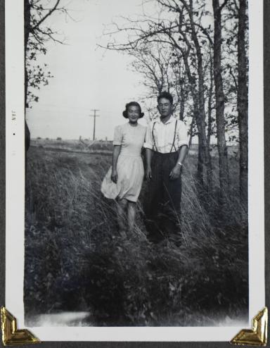 A young Japanese Canadian couple pose in a field with trees in the background. Partially obscured.