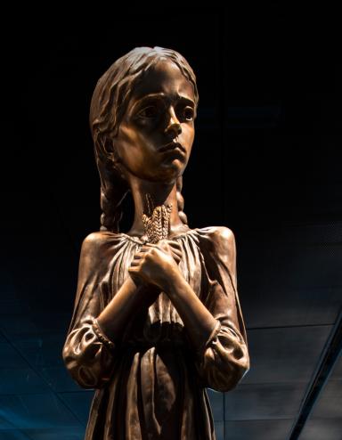 A statue of a girl holding stalks of wheat. Partially obscured.