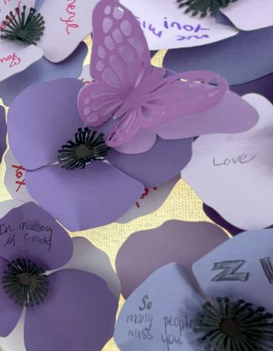 Purple poppies made of paper with names and messages from community members and family of those who have died as a result of a poisoned drug supply. Partially obscured.