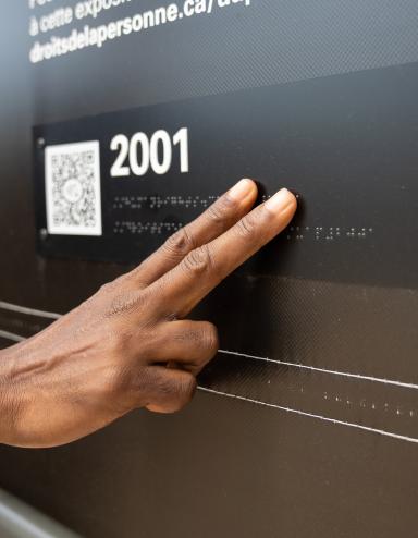 A hand touches braille letters on a museum exhibit.