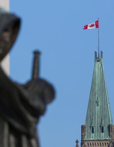 A Canadian flag flies atop a large tower. In the foreground stands a statue of a veiled woman carrying a sword.