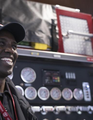 A smiling man stands in front of a fire truck.