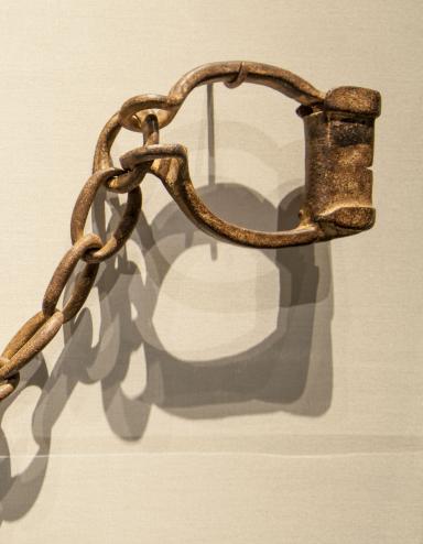 Rusted iron manacles hang on hooks on a plain white wall. 