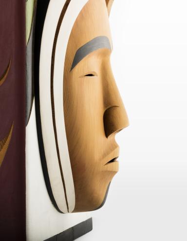 A closeup of a carved wooden box, showing the carved face of a person against a white background.
