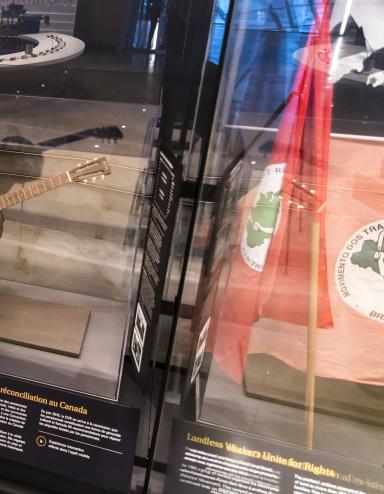 A row of museum display cases with various artifacts inside. A guitar is displayed under glass. The guitar has a colourful floral print with a bird hand-painted onto its front. Partially obscured.