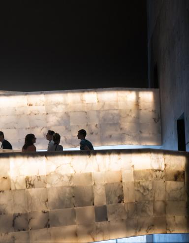 A group of people traveling up the Museum’s lighted alabaster ramps. Partially obscured.