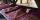 Stacks of three or four folded burgundy t-shirts lay on a wooden table.