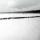 A black-and-white photo of a flat, snowy landscape with trees and small buildings in the distance. A long, straight line of more than 100 people are walking through snow.