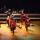 A drumming troupe dancing on a stage. The drums and parts of their costumes are a bright red.