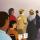 An illustration of people in line waiting to vote. The man in front places his ballot in the box on the table.