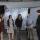 A small group of people stand in a semicircle in front of large screen displays.
