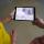 A young woman and a young man each hold one side of a tablet that shows the home page of the app called Proclamation 1982.