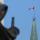 A Canadian flag flies atop a large tower. In the foreground stands a statue of a veiled woman carrying a sword.