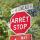 A stop sign and street sign in both English and French are seen in front of trees.