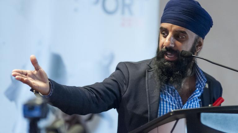 A head-and-shoulders image of Pardeep Singh Nagra speaking into a microphone at a podium. He is looking to his right and his right arm is extended out with his palm upturned.