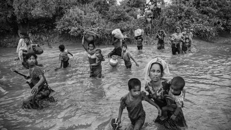 A group of Rohingya women and children carry their belongings as they wade across a canal filled with two to three feet of water.